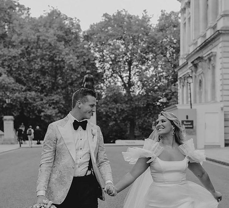 bride wearing a ruffle Halfpenny London wedding dress, while holding groom's hand on wedding day