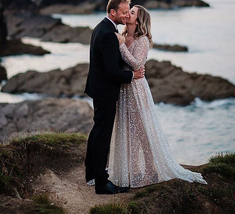 bride wearing a sparkly bespoke wedding dress by the sea on wedding day with groom