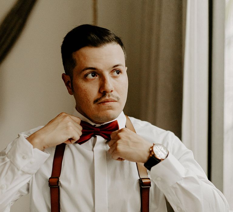 groom-getting-ready-for-wedding-with-dark-red-bow-tie