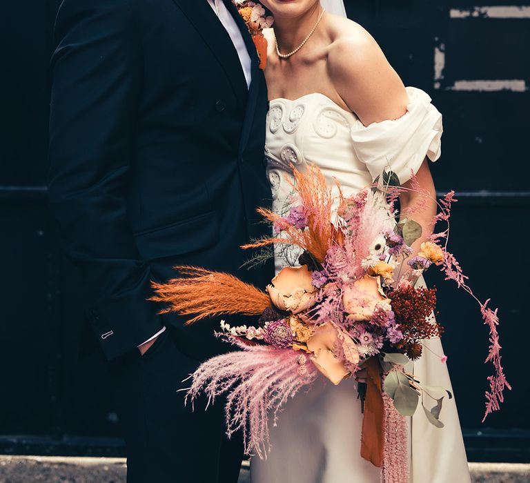 groom-in-black-tuxedo-with-bride-in-off-the-shoulder-wedding-dress-with-pampas-grass-wedding-bouquet