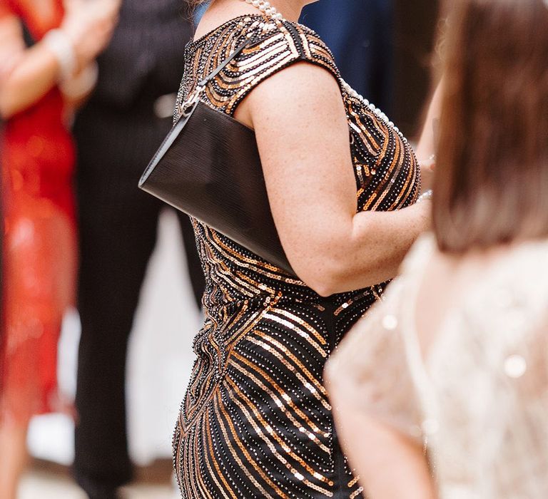 wedding guest wearing black and gold dress with feather headband