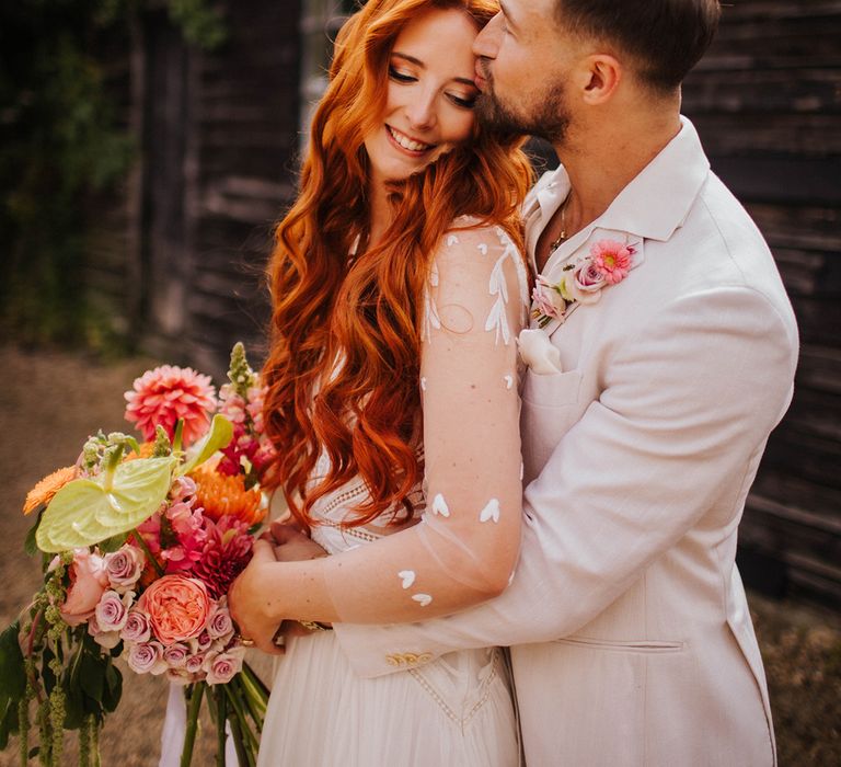 groom-in-white-suit-embracing-bride-in-long-sleeve-wedding-dress