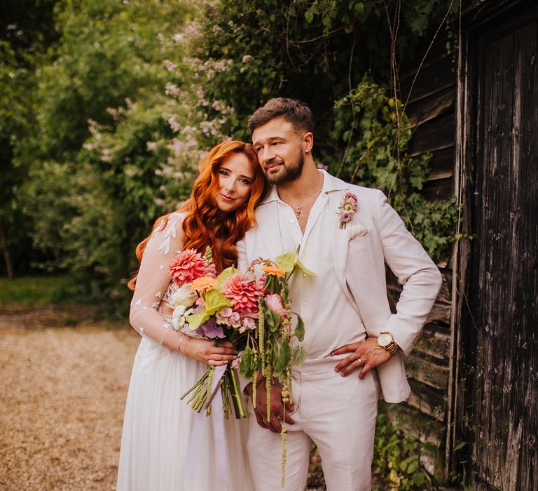 groom-in-white-suit-with-bride-holding-pink-wedding-bouquet