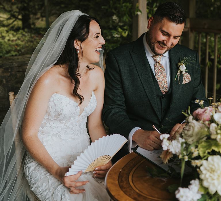 bride-in-floral-lace-strapless-wedding-dress-with-groom-in-green-suit-at-outdoor-wedding