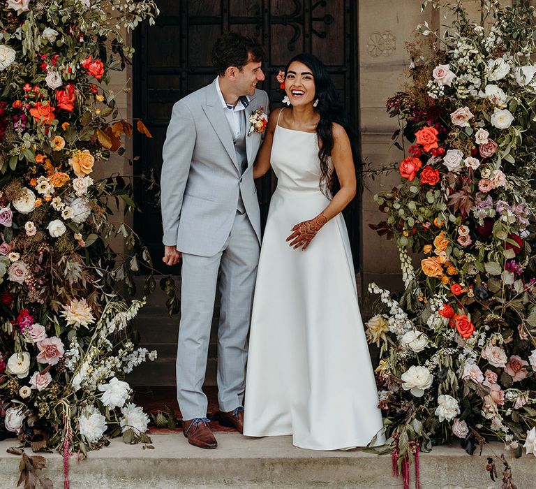 bride-and-groom-laughing-for-couple-portrait-with-colourful-entrance-flowers