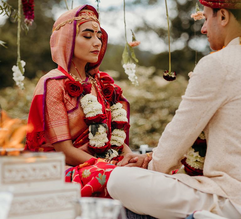 bride-wearing-red-and-gold-wedding-outfit-with-varmala-garland