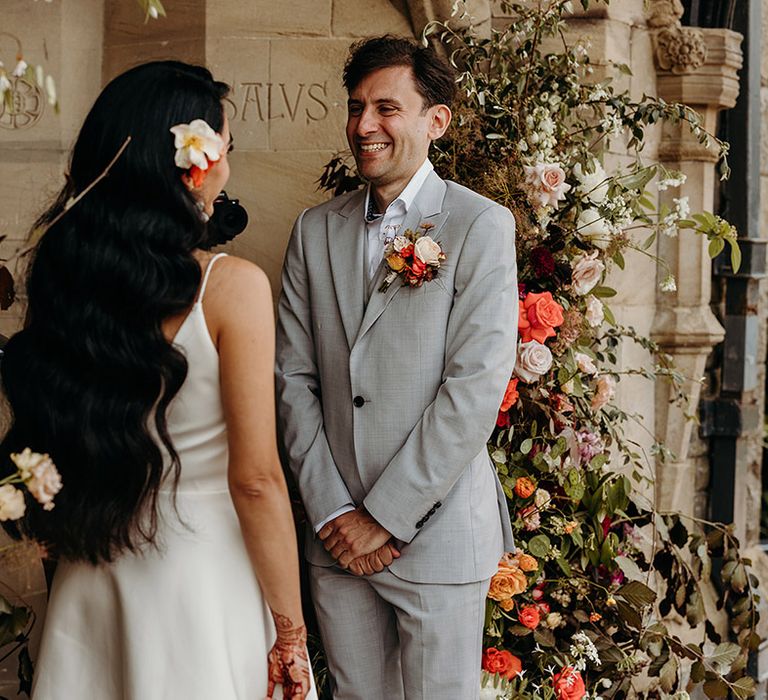 bride-with-long-wavy-hair-with-flower-accessory-smiling-at-groom-in-grey-suit