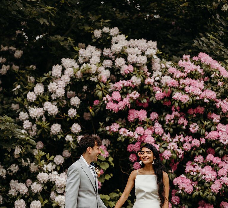 stunning-pink-flowers-in-garden-with-bride-and-groom-holding-hands-for-couple-portrait