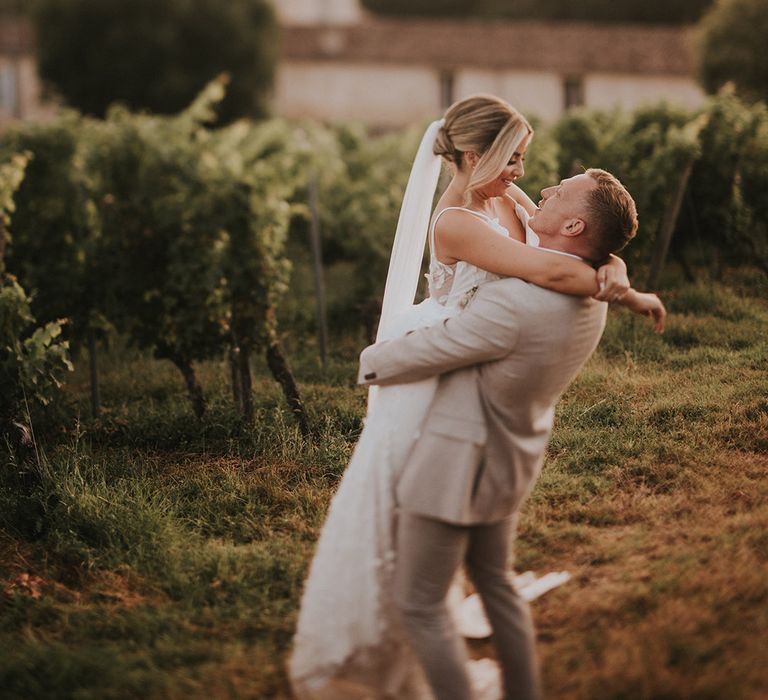 groom-in-light-beige-wedding-suit-embracing-bride-with-veil