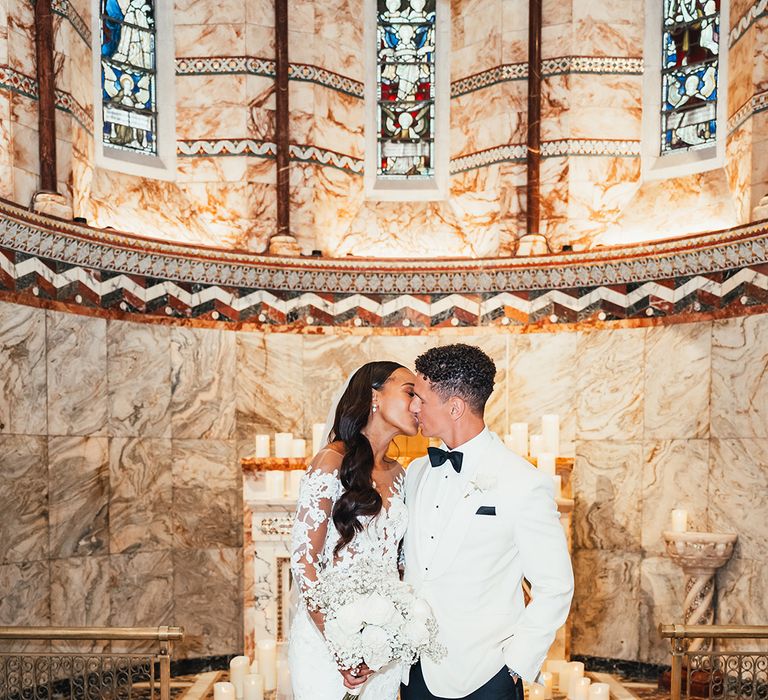 groom-in-white-tuxedo-kissing-bride-in-lace-wedding-dress