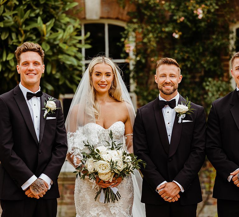 groomsmen-wearing-black-tuxedos-with-bride-in-lace-wedding-dress