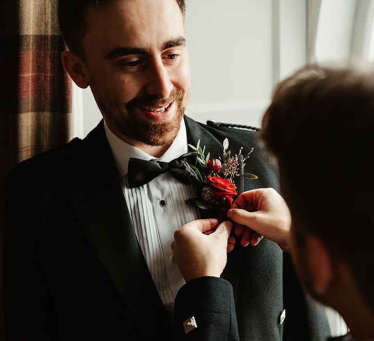 groom-gets-red-rose-buttonhole-put-on-suit-jacket