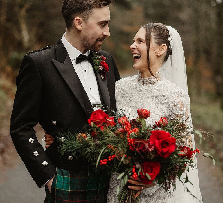 lace-wedding-dress-worn-by-bride-holding-red-rose-wedding-bouquet-with-groom-in-black-tie