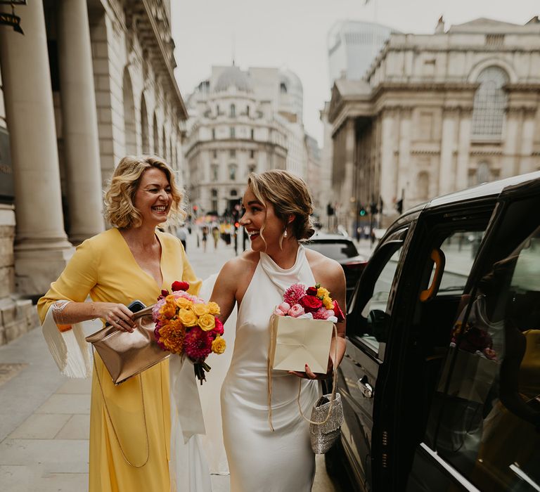 bride-in-satin-wedding-dress-with-wedding-guest-in-yellow-dress-next-to-black-cab