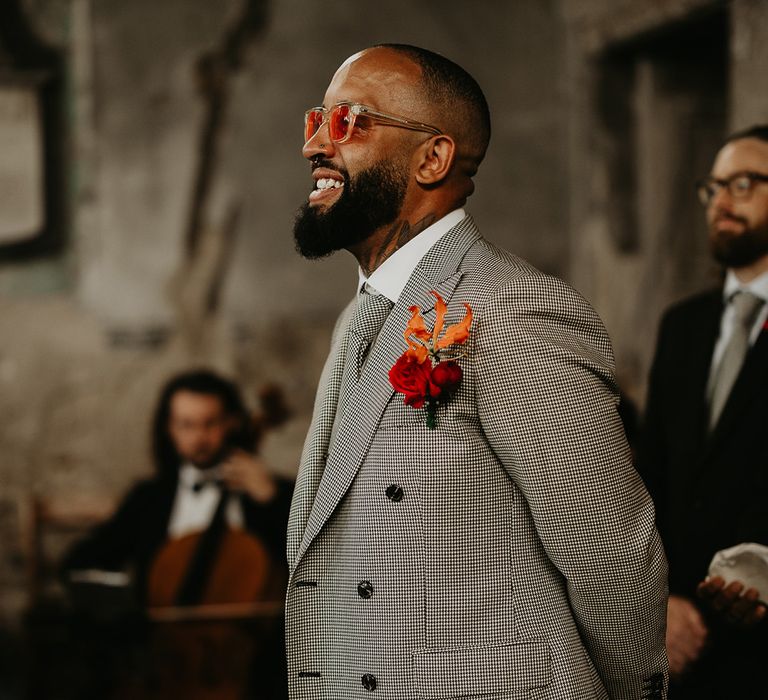 groom-wearing-grey-wedding-suit-with-pink-rose-buttonhole-and-colourful-glasses