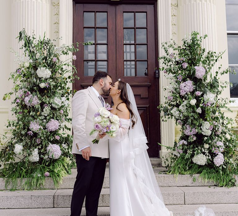 bride-and-groom-kiss-at-hawkstone-hall-with-purple-column-flowers