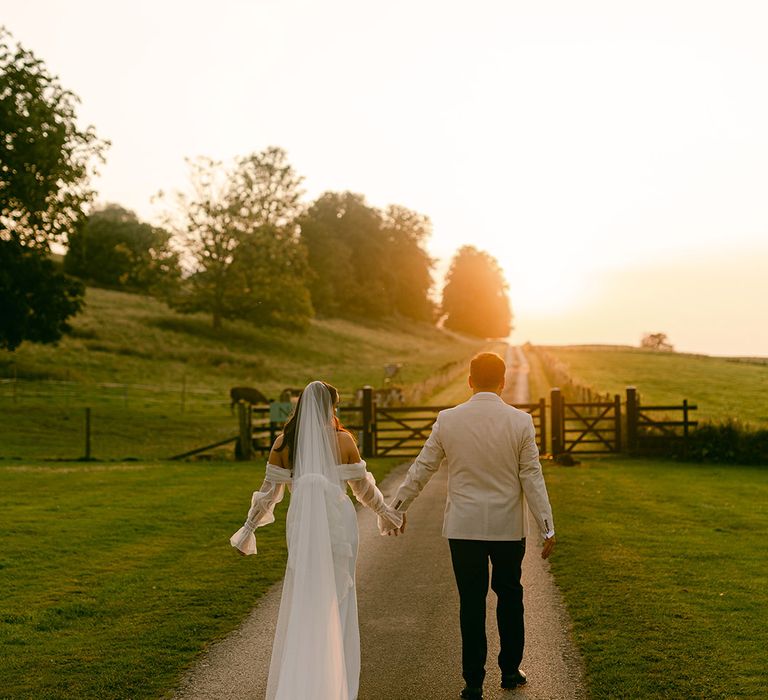 golden-hour-wedding-photo-of-bride-and-groom-walking-hand-in-hand