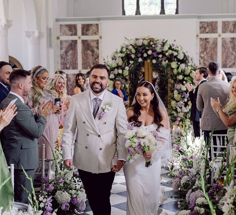 groom-in-double-breasted-suit-walking-with-bride-back-down-the-aisle