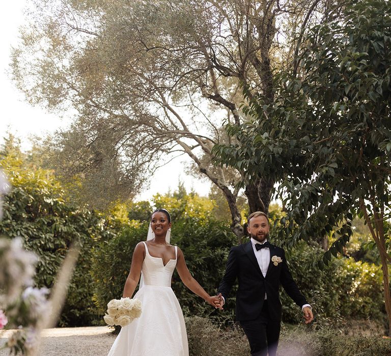 bride-and-groom-walking-hand-in-hand-wearing-black-tuxedo