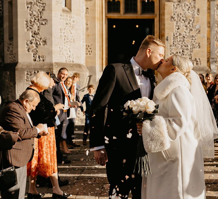 bride-in-faux-fur-coat-kissing-groom-at-intimate-wedding