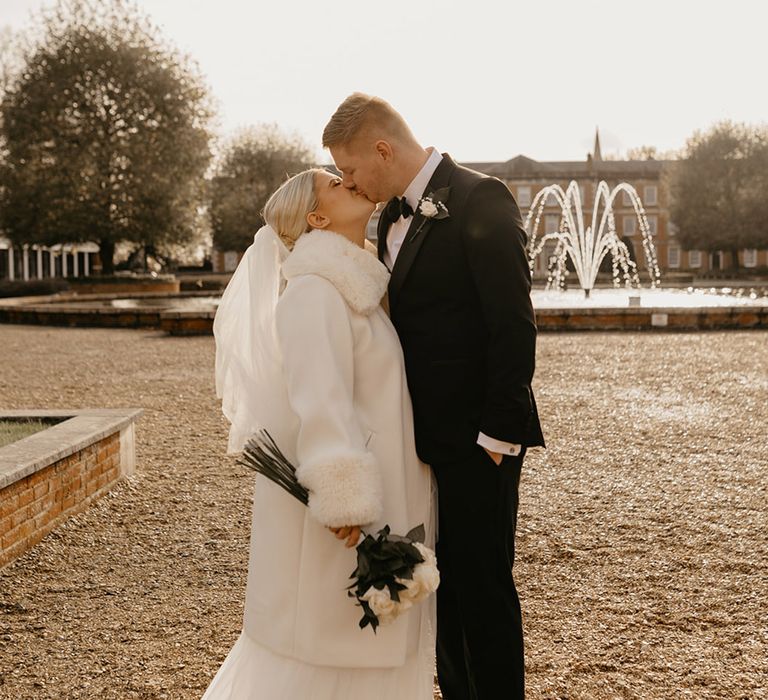 bride-wearing-white-faux-fur-coat-kissing-groom-at-winter-wedding