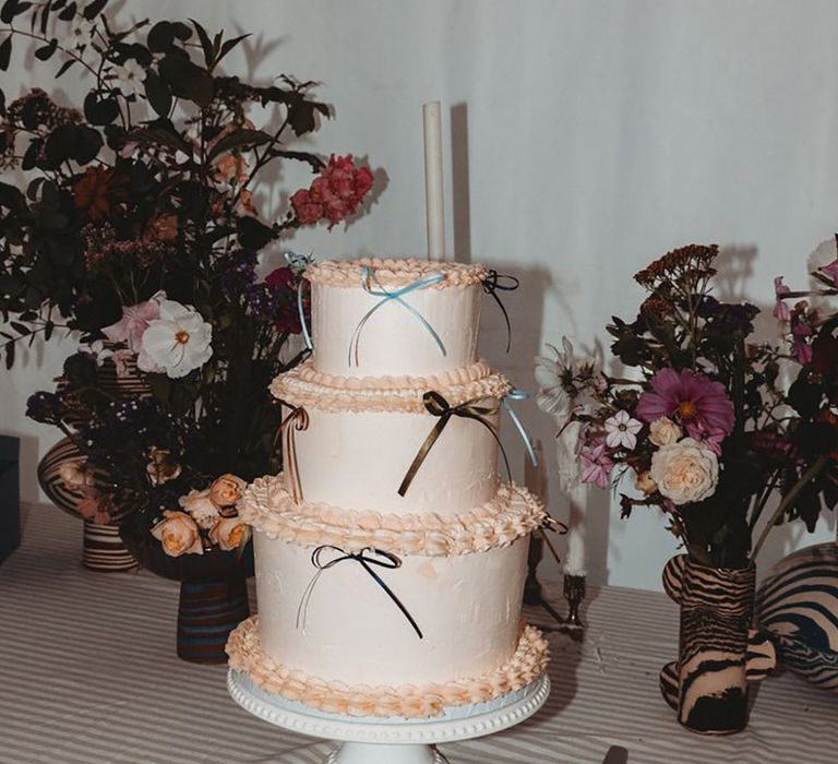 Three tier iced wedding cake with peach icing decorated with wedding bows