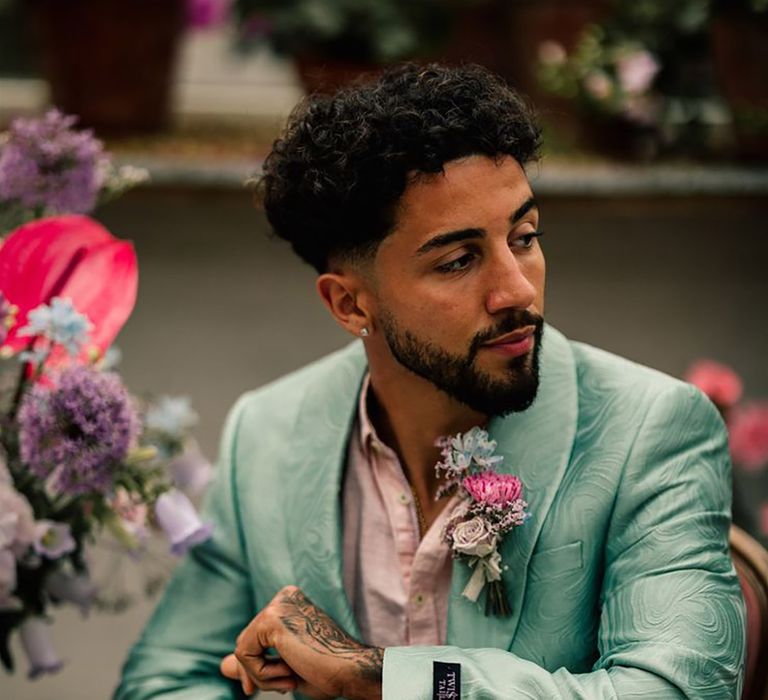 groom wearing a mint green swirl pattern suit jacket with floral print trousers and a pale pink shirt with pink flower buttonhole