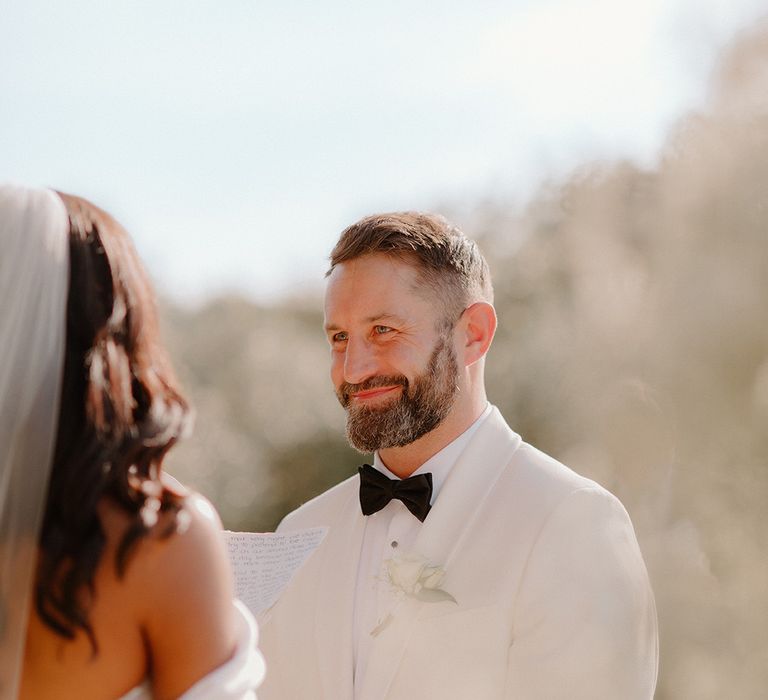 groom-in-white-tuxedo-exchanging-vows-with-bride