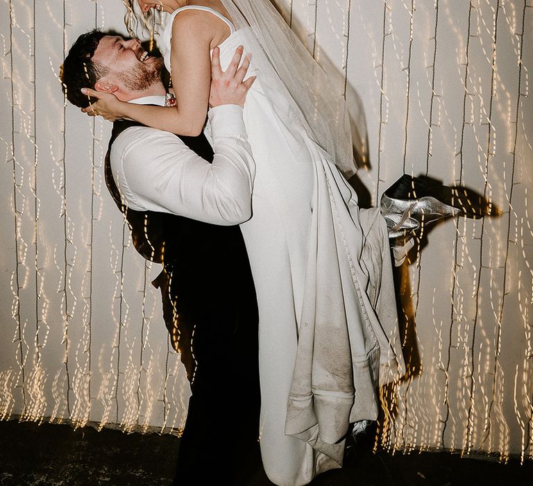 groom-lifting-bride-at-wedding-reception-with-fairy-lights