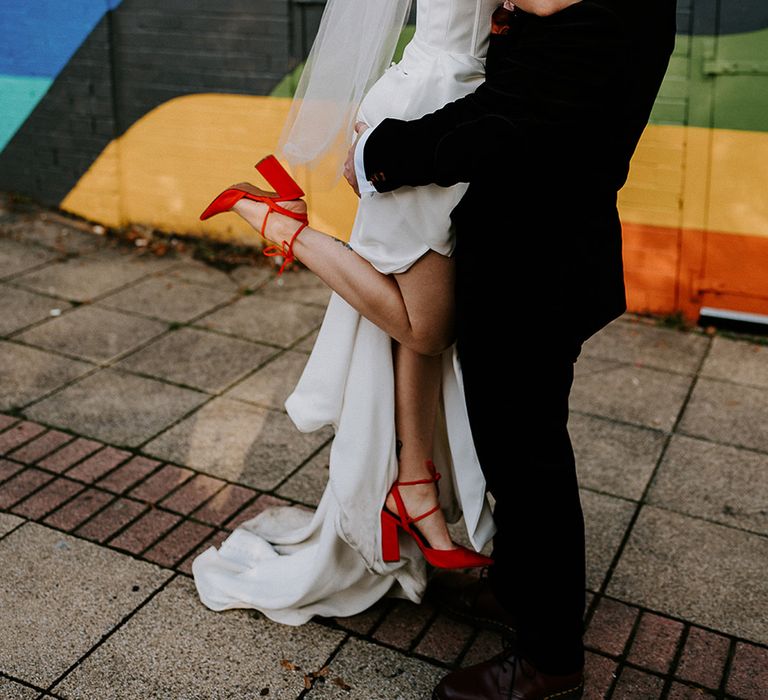 groom-lifts-bride-for-romantic-wedding-photo-in-front-of-colourful-backdrop