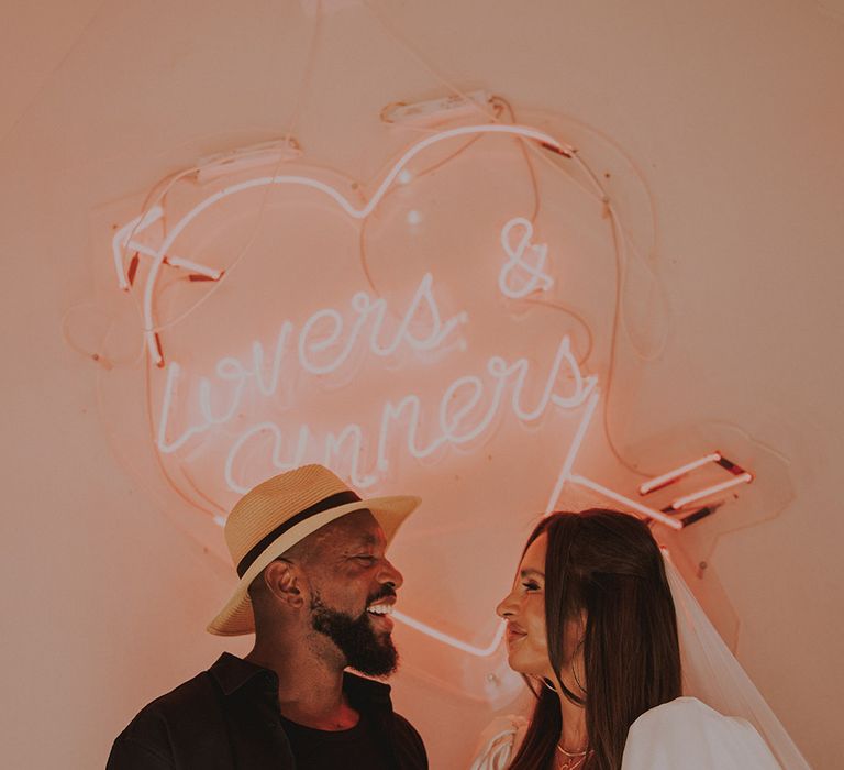 heart-neon-sign-with-groom-in-hat-smiling-at-bride