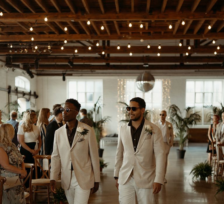 groomsmen-walk-down-the-aisle-wearing-black-shirts-and-cream-suit-jackets