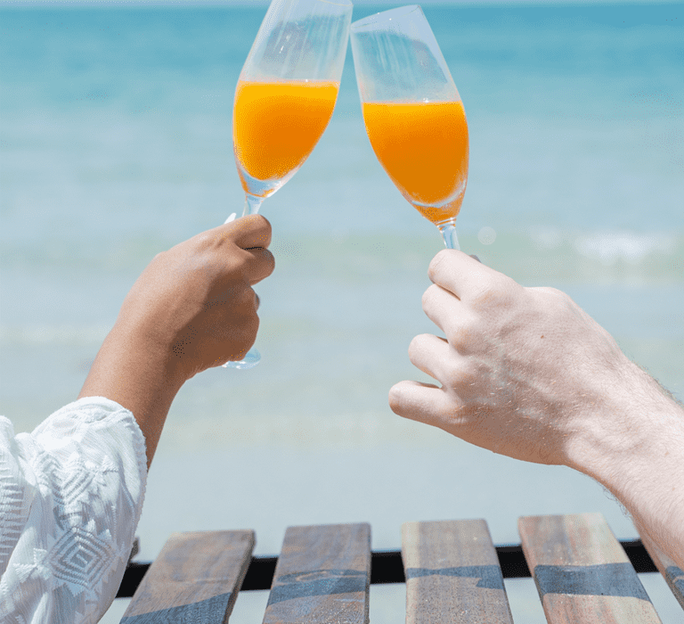 Couple toasting with cocktails on the beach, celebrating their honeymoon.