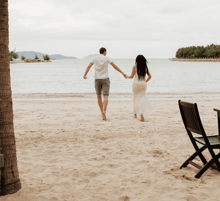 couple joyfully running along the beach towards the sea, celebrating their honeymoon