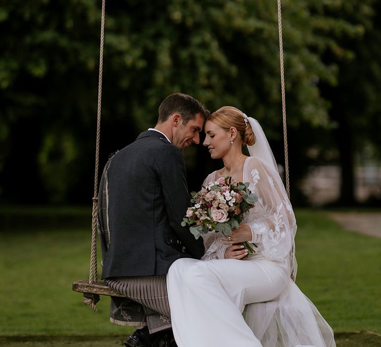 bride-wearing-long-sheer-sleeve-wedding-dress-on-wooden-swing-with-groom