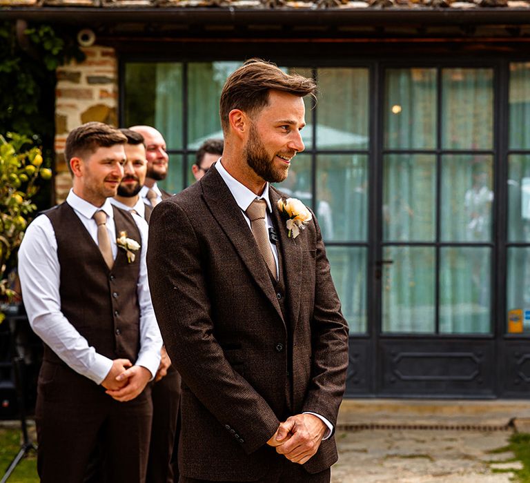 groom-wearing-brown-wedding-suit-waiting-at-ceremony-to-see-bride