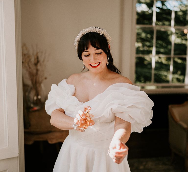 bride-wearing-off-the-shoulder-statement-wedding-dress-putting-on-wedding-perfume