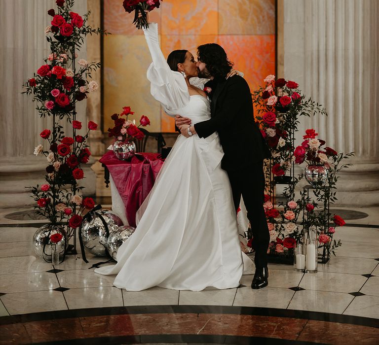groom-kisses-bride-in-celebration-with-bride-holding-bouquet-in-the-air