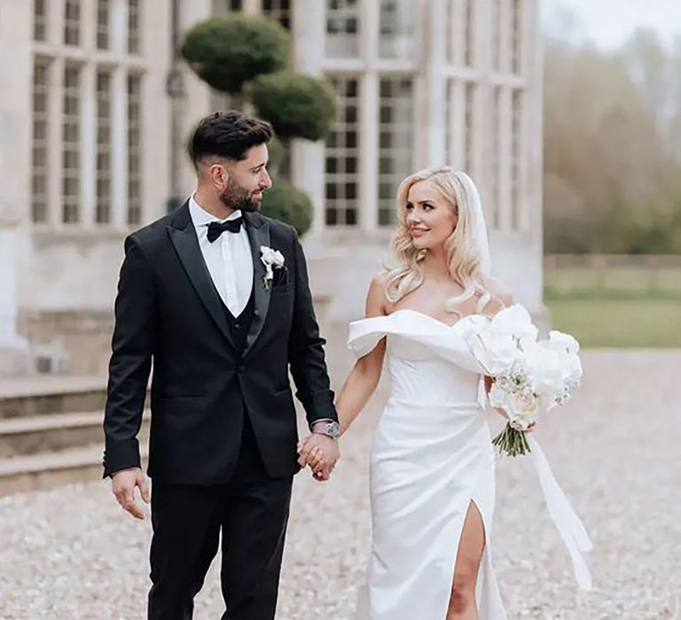 bride holding grooms hand while wearing glamorous off-shoulder wedding dress with leg slit 