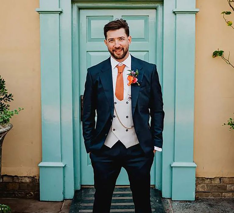 groom wearing three piece wedding suit with orange tie 