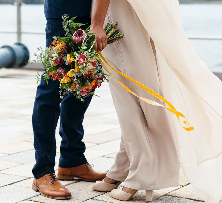 Bride in Bespoke Ailsa Monroe Jumpsuit & Cape | Groom in Next Navy Wool Suit | Relaxed Industrial Wedding at Ocean Studios, Plymouth | Freckle Photography