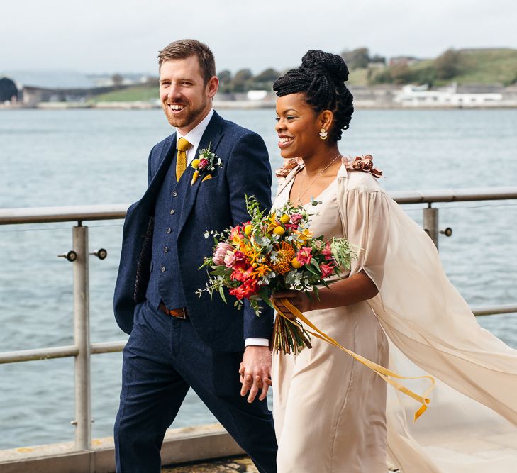 Bride in Bespoke Ailsa Monroe Jumpsuit & Cape | Groom in Next Navy Wool Suit | Relaxed Industrial Wedding at Ocean Studios, Plymouth | Freckle Photography