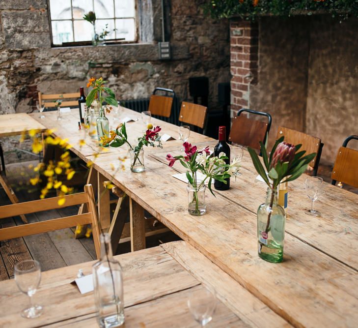 Trestle Tables with Flower Stems in Bottles | | Relaxed Industrial Wedding at Ocean Studios, Plymouth | Freckle Photography