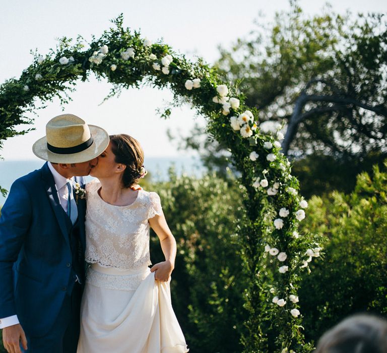 Bride in Verónica Miranda Bridal Separates & Groom in Navy Suit by The Fitters Under Floral Arch