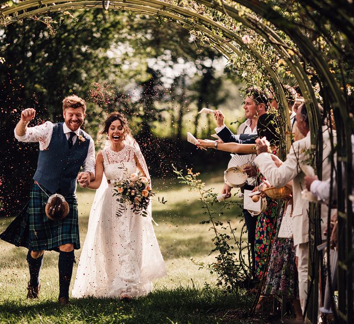 Confetti Exit | Bride in Lace Yolan Cris Gown | Groom in Tartan Kilt | Outdoor Destination Wedding at Château De Malliac Planned by Country Weddings in France | Styling by The Hand-Painted Bride | Samuel Docker Photography | Marriage in Motion Films