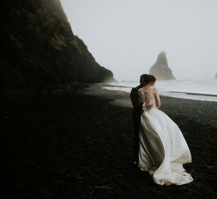 Portrait of wedding couple with backs to the camera on a black sand beach