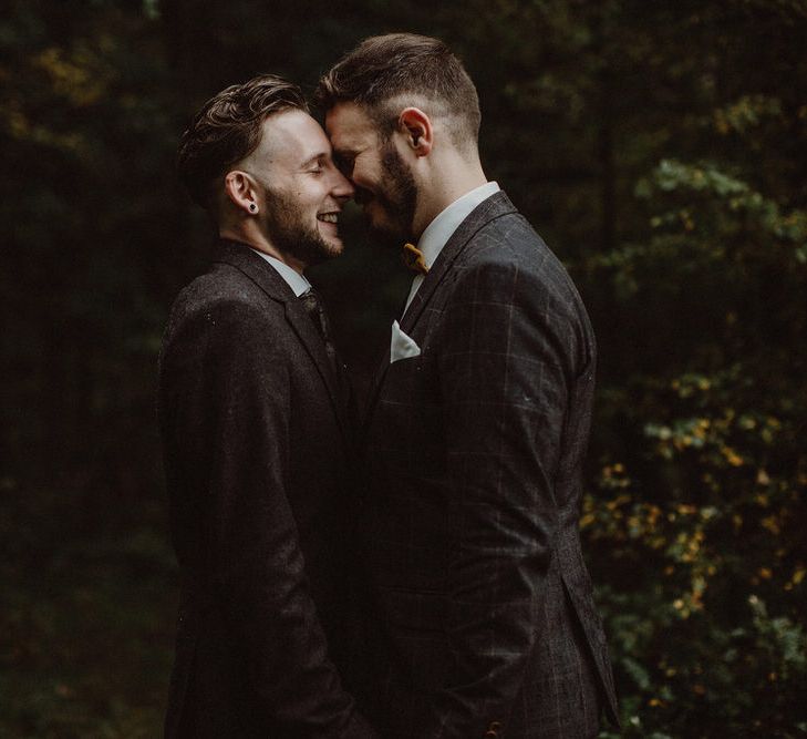 Two grooms stand with foreheads together smiling in dark wedding photo