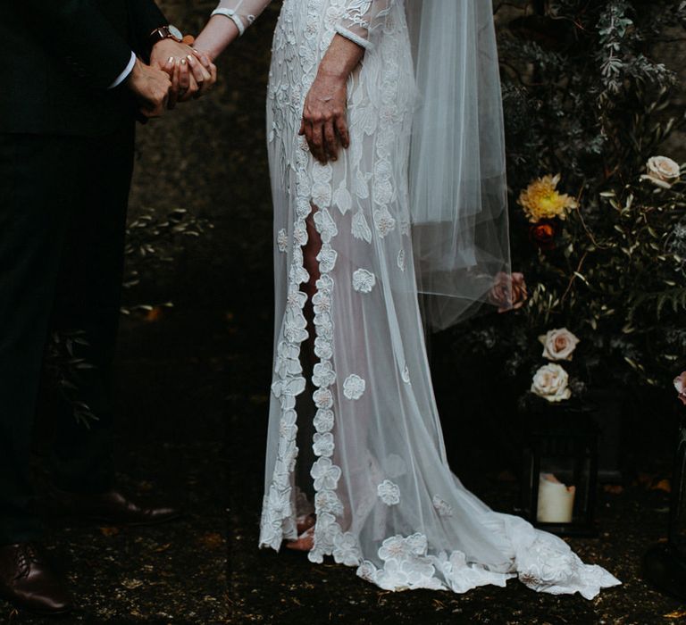 Bride in split leg lace wedding dress holding hands with groom in black suit - Moody & Dark Wedding Photographer