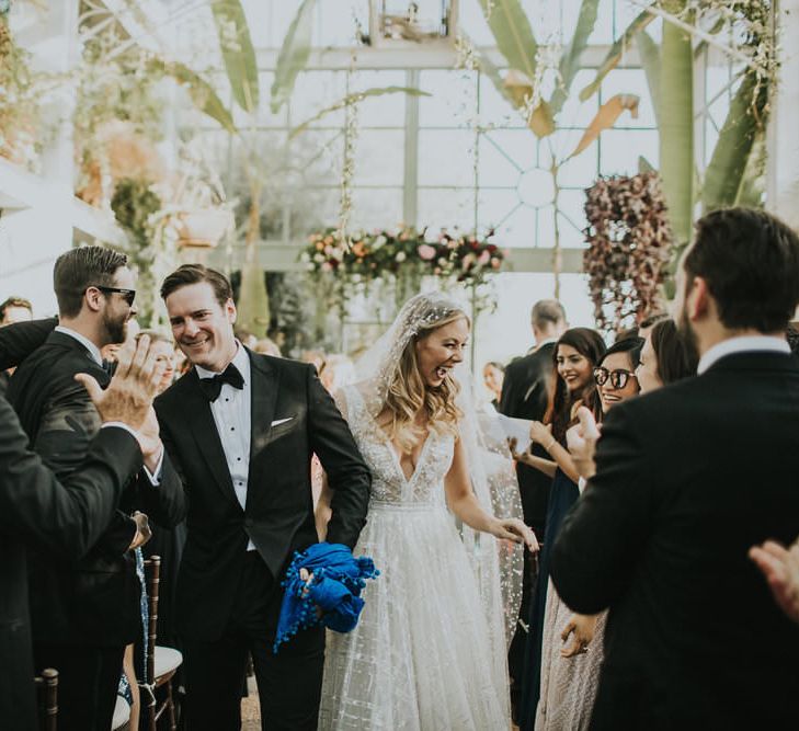 Bride and groom exit wedding ceremony high fiving guests