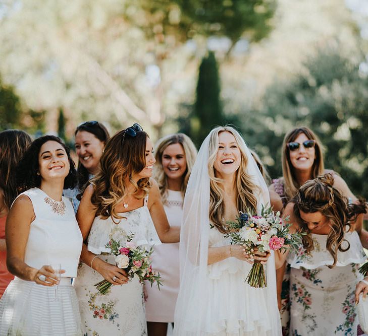 White bride with full length veil holds pink bouquet and laughs with bridesmaids